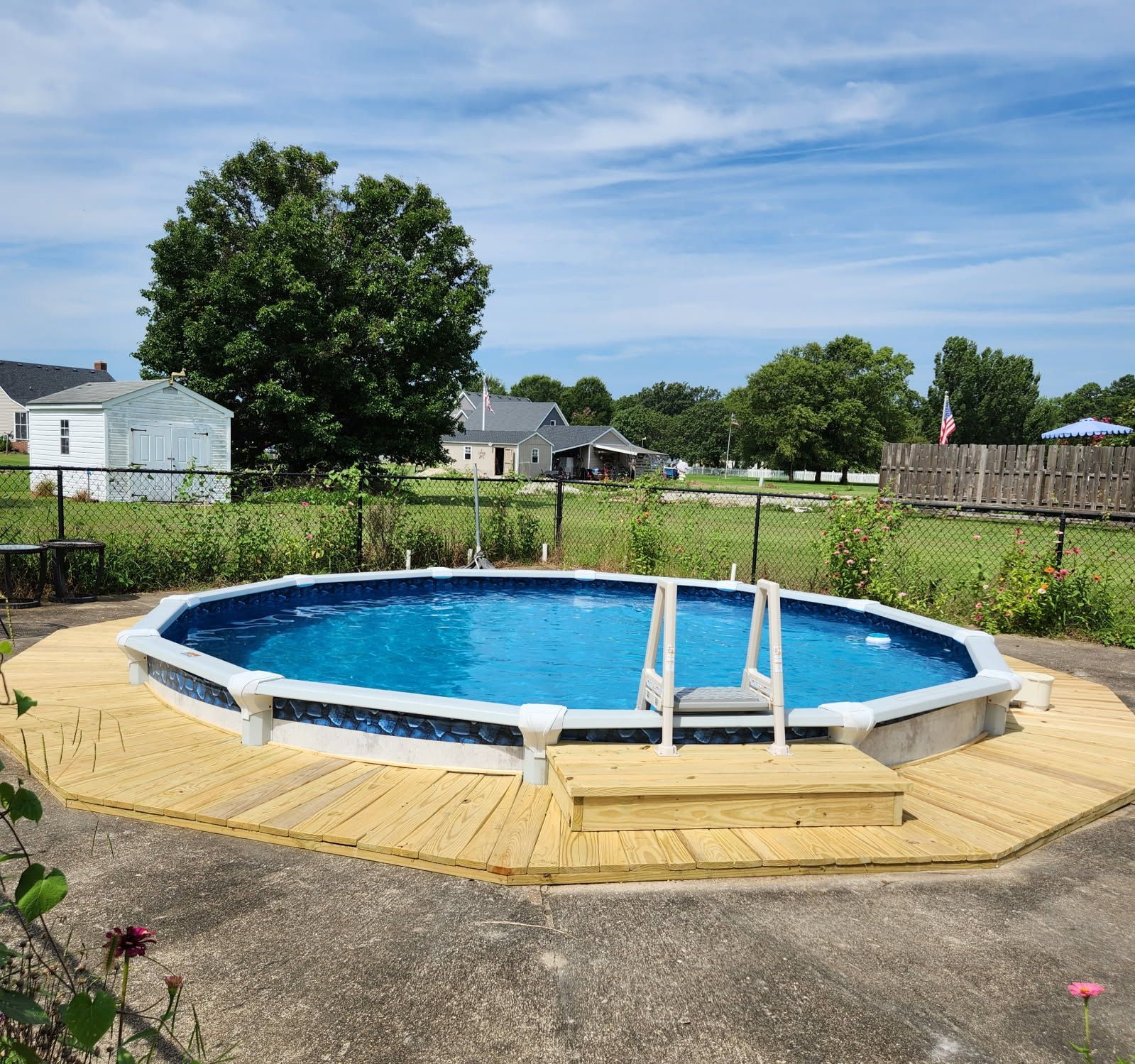 Above-ground backyard pool with blue water, white ladder, and yellow deck in a fenced yard