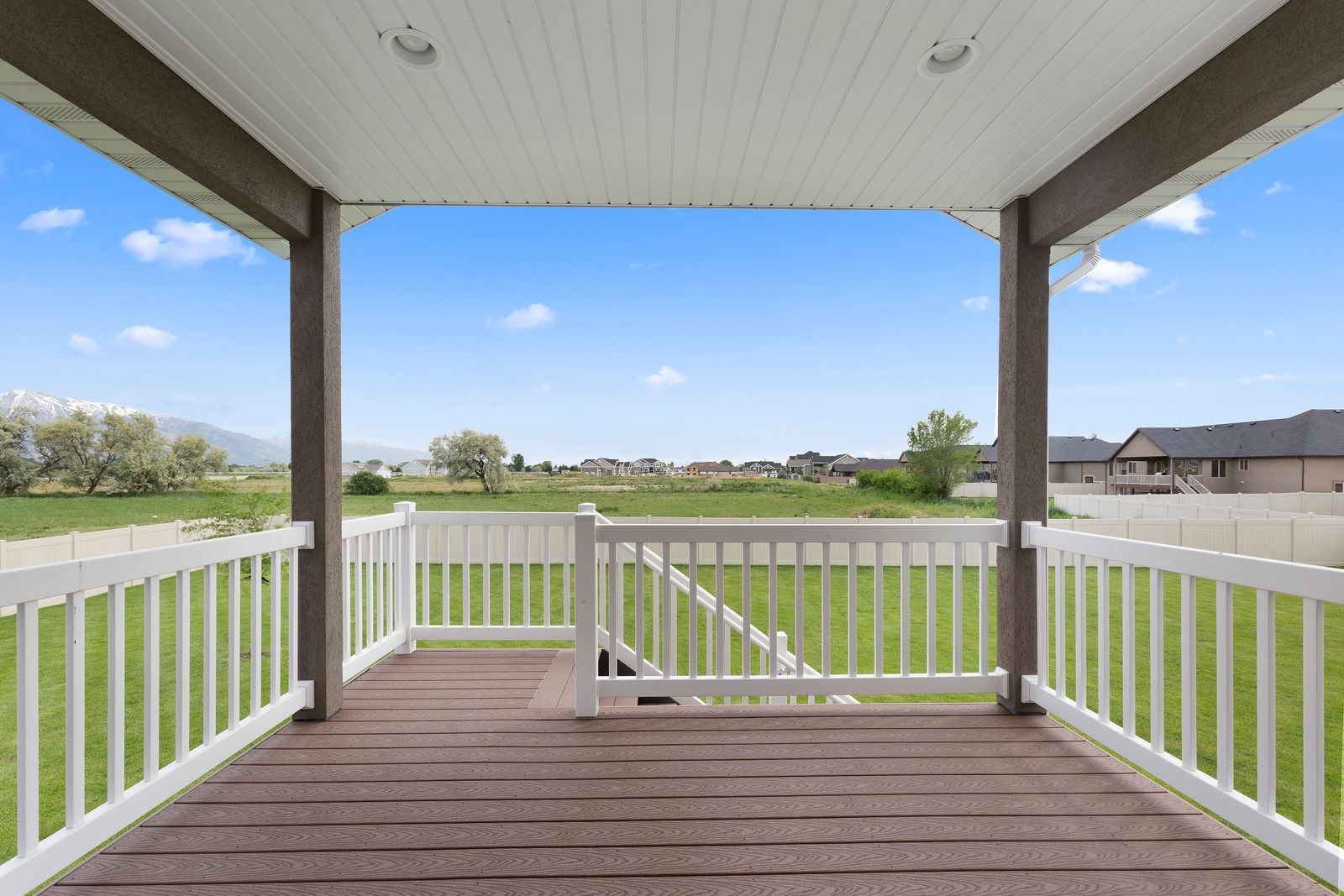 An empty porch with a white railing and a view of a field.