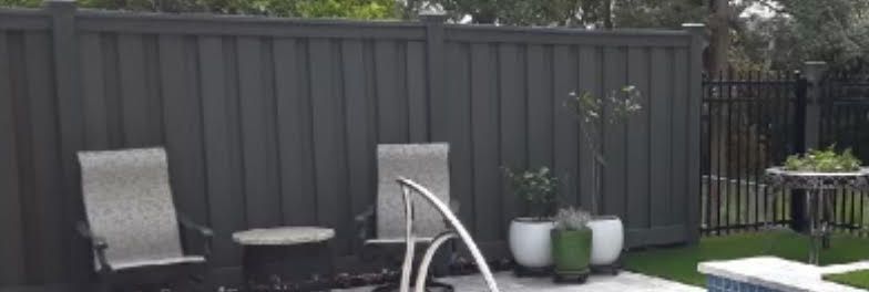 Backyard patio with gray fence, two chairs, small table, and potted plants on a green lawn