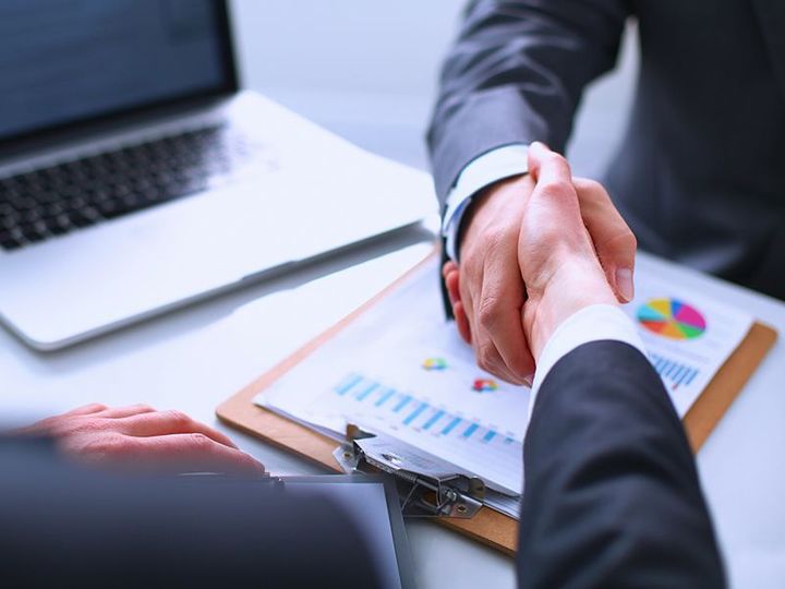 Business handshake over reports beside a laptop and colorful charts