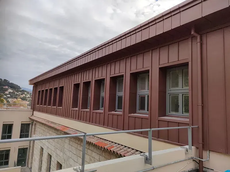 Bâtiment aux façades et fenêtres en métal brun, sous un ciel couvert.