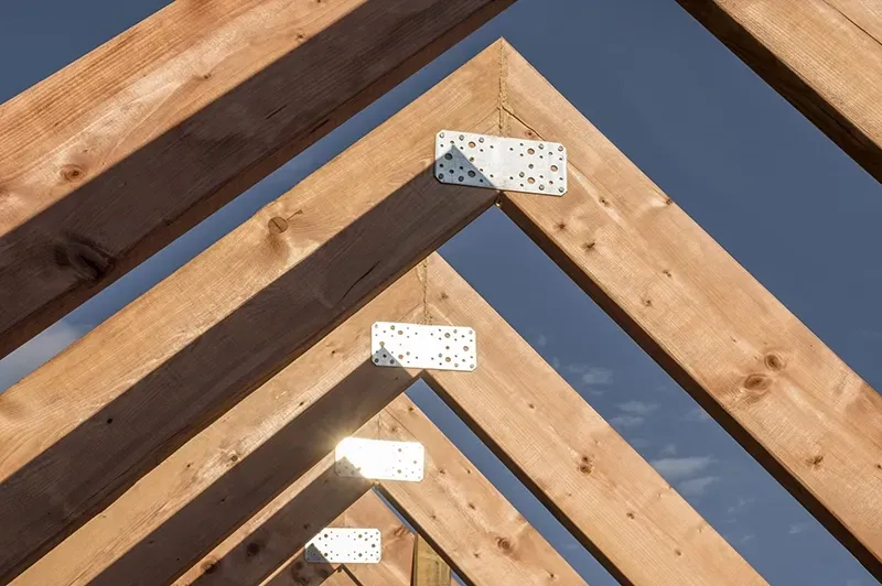 Charpente de toit en bois assemblée par des connecteurs métalliques sur fond de ciel bleu.