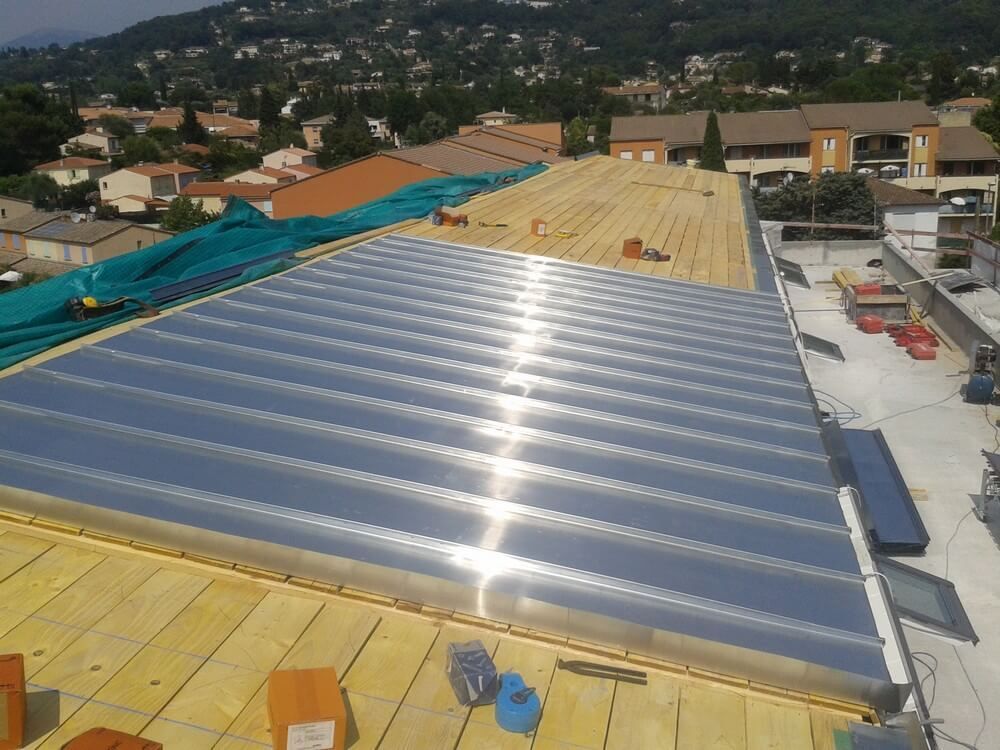 Toiture en construction, montrant l'installation de panneaux métalliques sur une charpente en bois, avec une colline au loin.