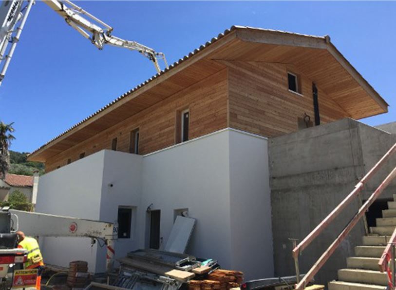 Chantier de construction d'un bâtiment au toit en bois et aux murs blancs. Pompe à béton depuis le haut.