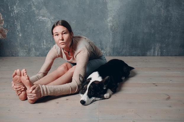 mulher se alongando com cachorro deitado ao lado no chão