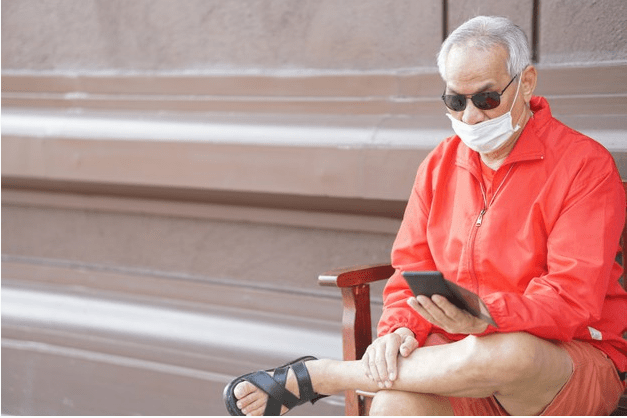 senhor sentado em banco com celular e mascara 