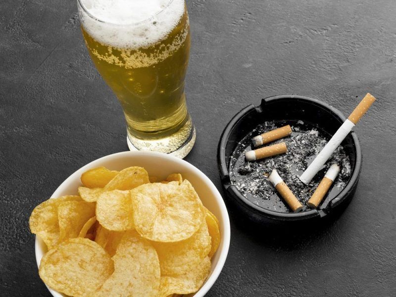 Copo de cerveja e cigarros sobre uma mesa, representando contraste entre hábitos saudáveis e nocivos.