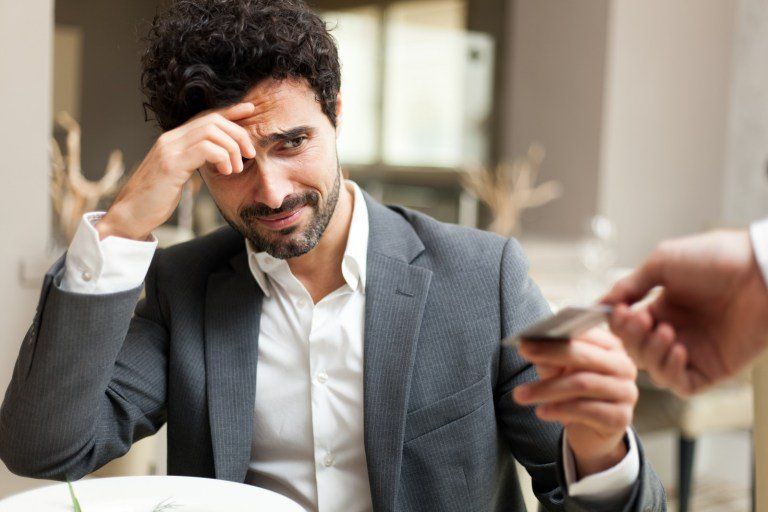 homem com expressão de receio ao entregar o cartão para pagar