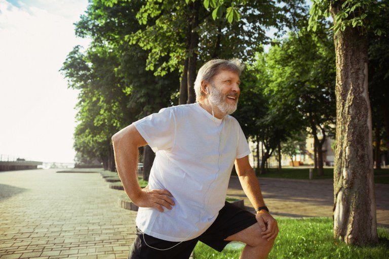 Homem idoso caminhando em parque com expressão feliz, segurando a lateral do corpo