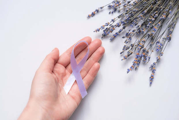  Mão segurando laço roxo ao lado de um ramo de lavanda, simbolizando o Dia Roxo de conscientização sobre a epilepsia.
