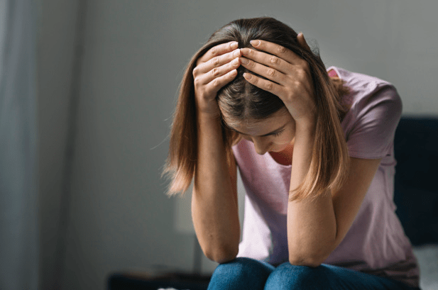 mulher sentada com as mãos na cabeça olhand para baixo