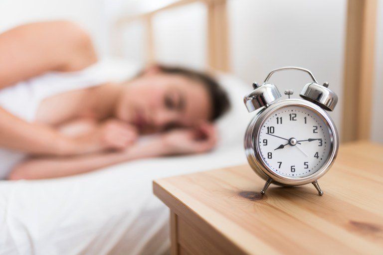 mulher dormindo desfocada com despertador a frente