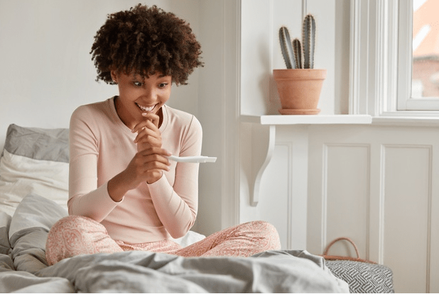 mulher na cama com teste de gravidez, feliz