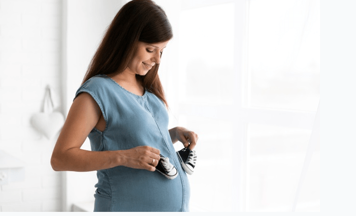 mulher gravida com sapatinhos de bebê sobre a barriga