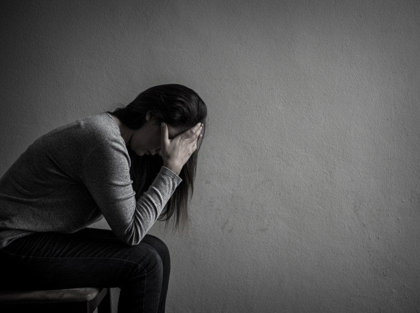 mulher sentada com mãos na cabeça com fundo cinza