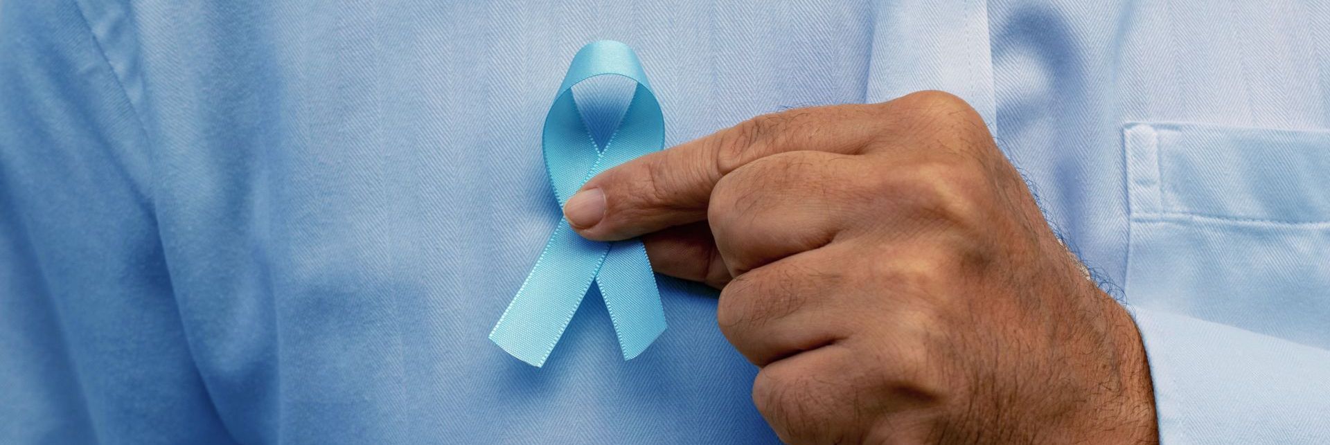 Mão masculina segurando laço azul, símbolo da campanha de prevenção ao câncer de próstata.