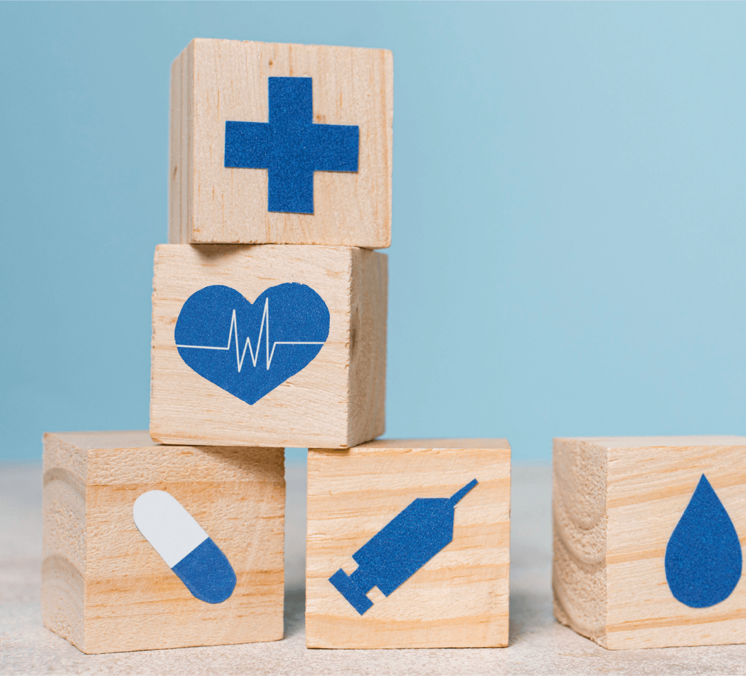 Cubos empilhados com ícones médicos como coração, pílula e cruz, sobre fundo azul claro.
