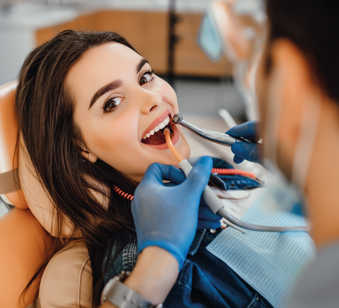 Jovem mulher em cadeira odontológica sendo examinada, com foco em sua expressão positiva e descontraída.
