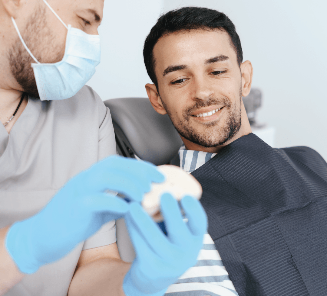 Paciente sorridente em consulta odontológica com dentista mostrando molde dentário.