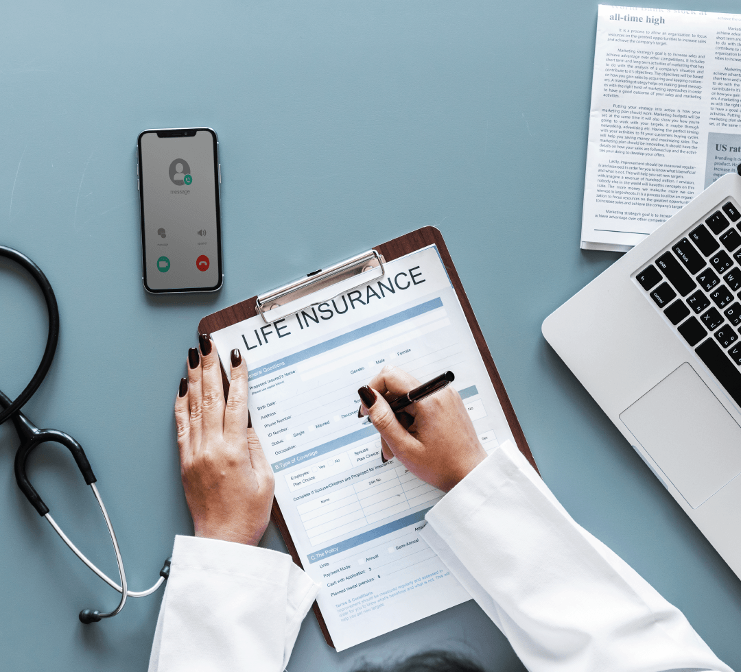 Pessoa preenchendo formulário de seguro ou plano de saúde, com estetoscópio, celular e notebook ao redor.