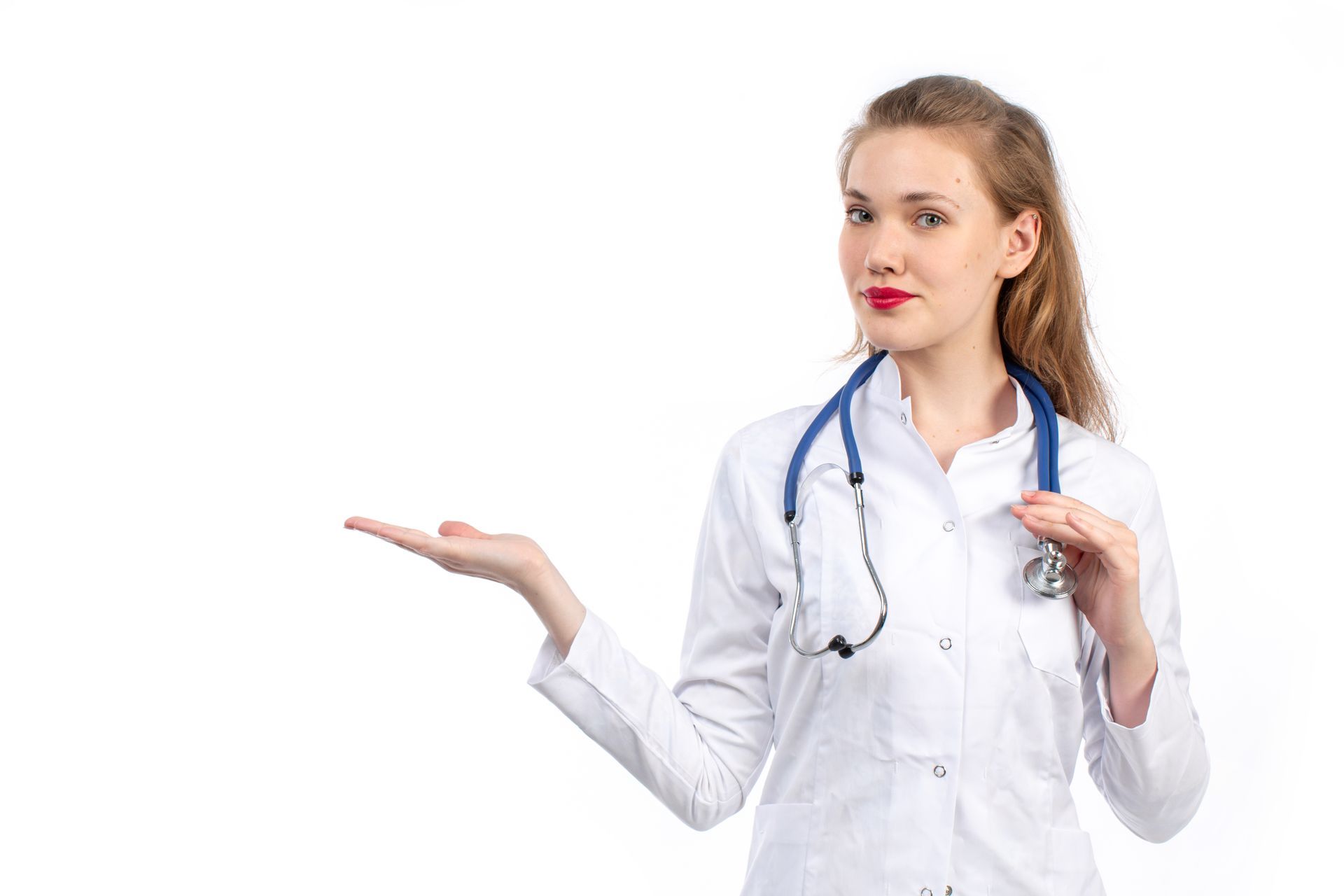 Jovem médica de jaleco branco com estetoscópio no pescoço, apontando para o lado, em fundo branco.