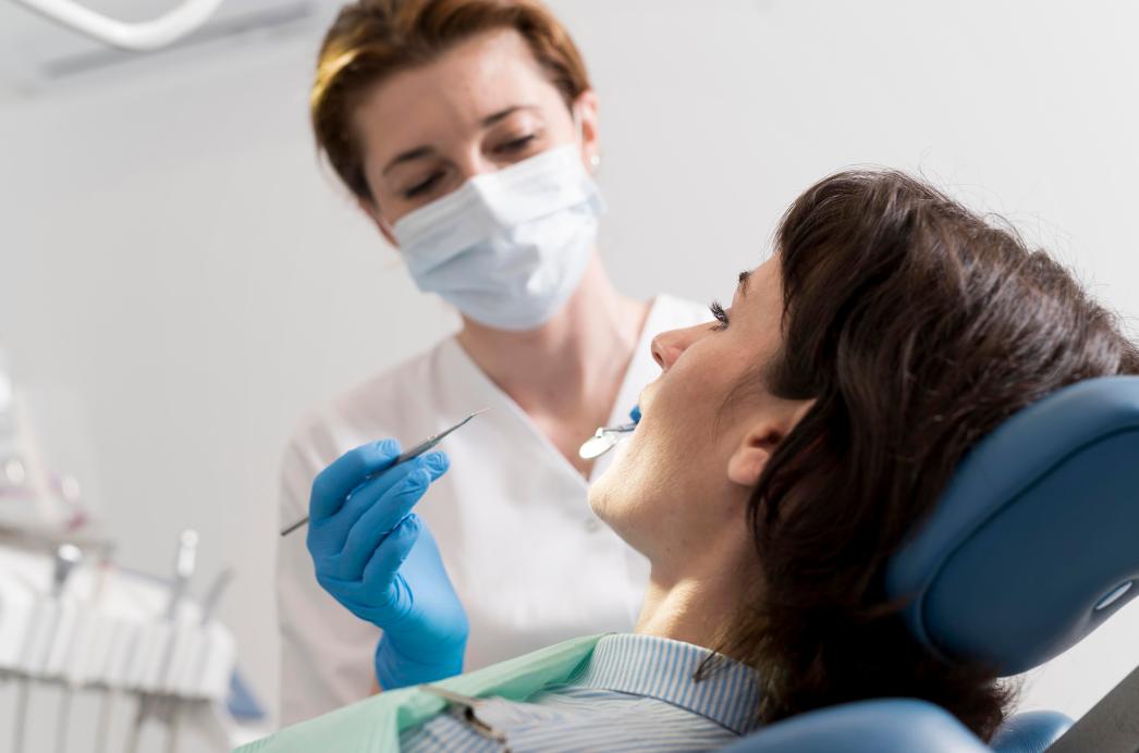 Jovem paciente sendo atendida por uma dentista em consultório, com foco na interação durante um procedimento odontológico.