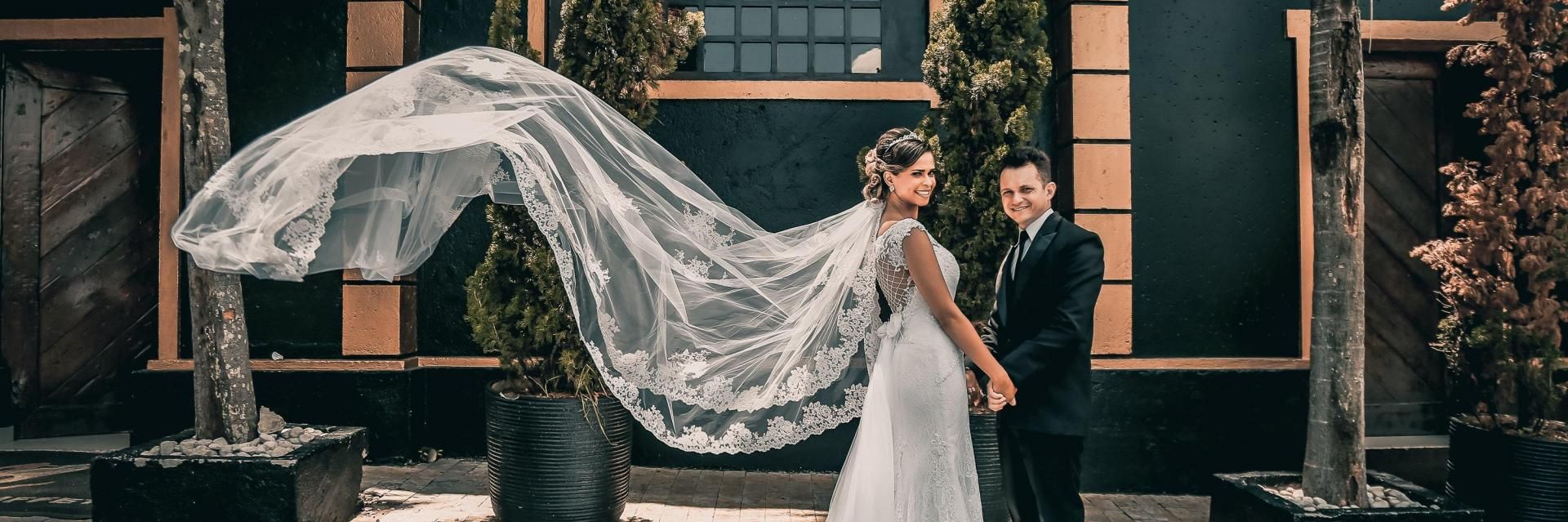 Bride and groom posing outdoors, with the bride’s veil billowing in the wind