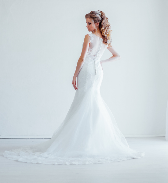 Woman in a white lace wedding dress posing in profile against a plain white background