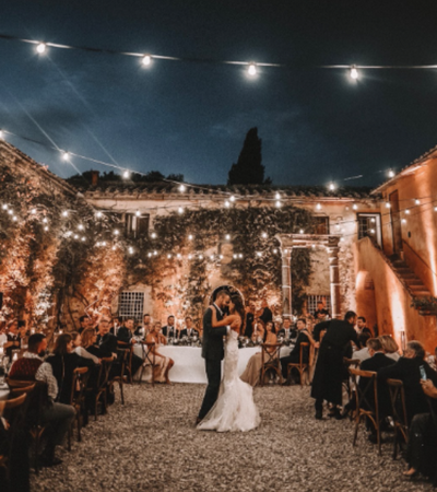 Bride and groom dancing at an outdoor evening wedding reception with string lights and guests seated nearby