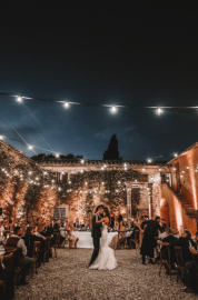 Bride and groom dancing under string lights at an outdoor evening wedding reception