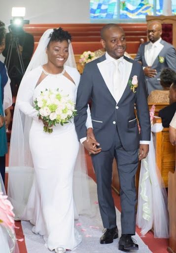 Bride and groom walking down the aisle, holding hands, with bouquets and wedding guests in the background