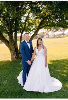Bride and groom posing under a large tree in a sunny park