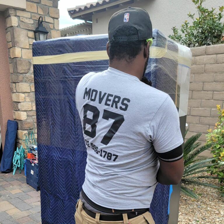 Man moving wrapped furniture outside a house; blue padding and yellow tape.