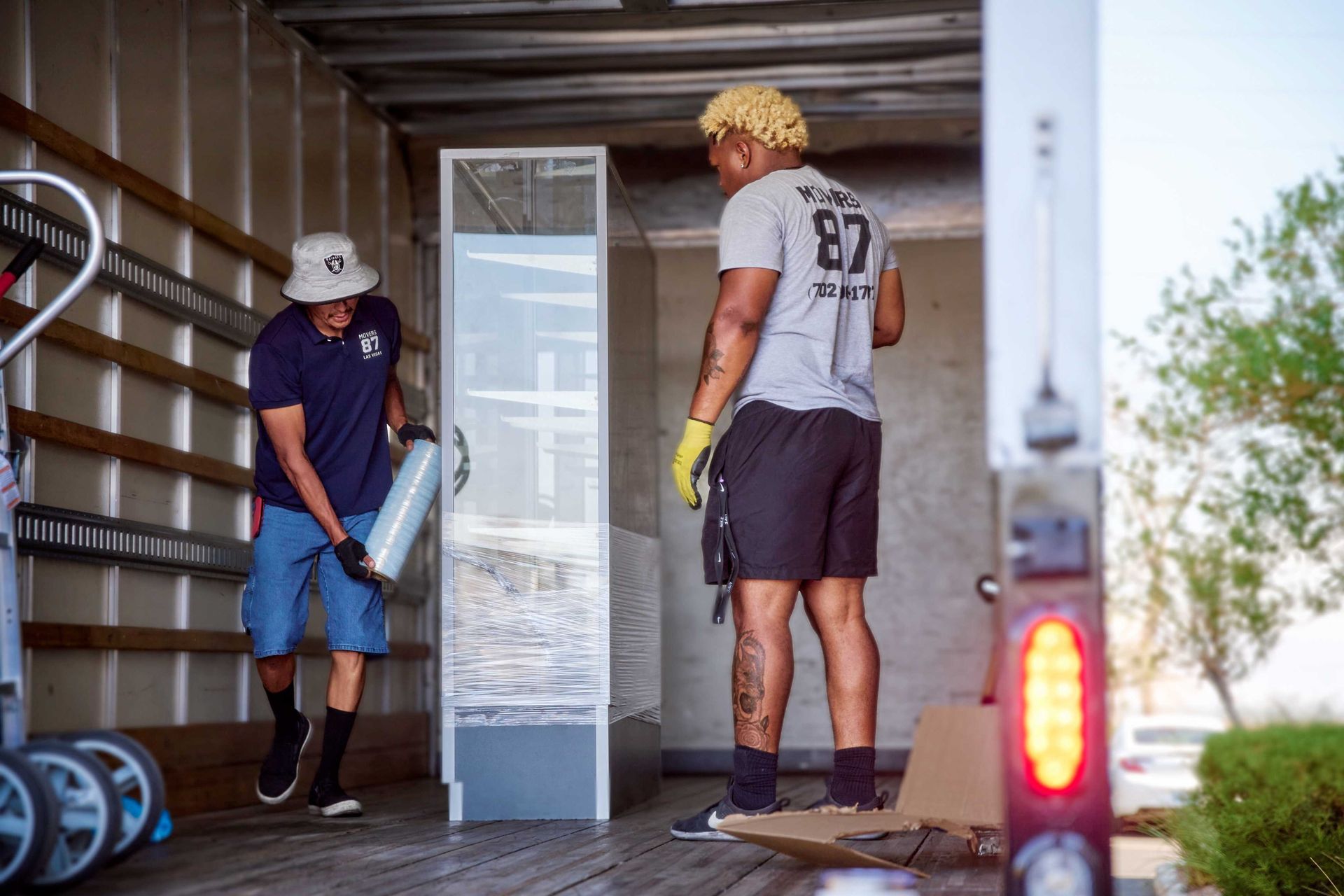 Two people loading a large, wrapped glass object into a truck. One is holding a cylindrical object.