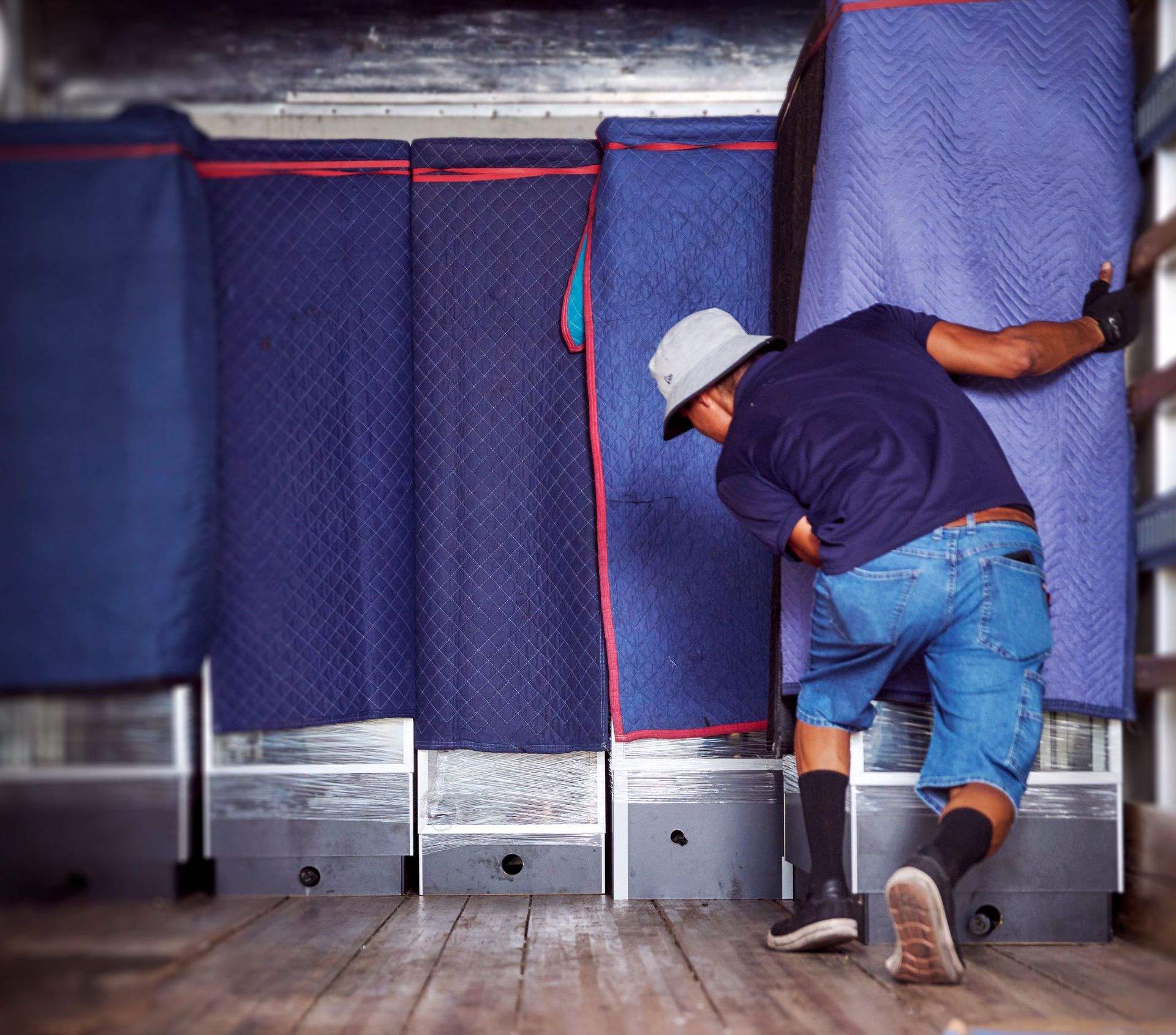 Man moving furniture, wrapped in blue padding, inside a truck.