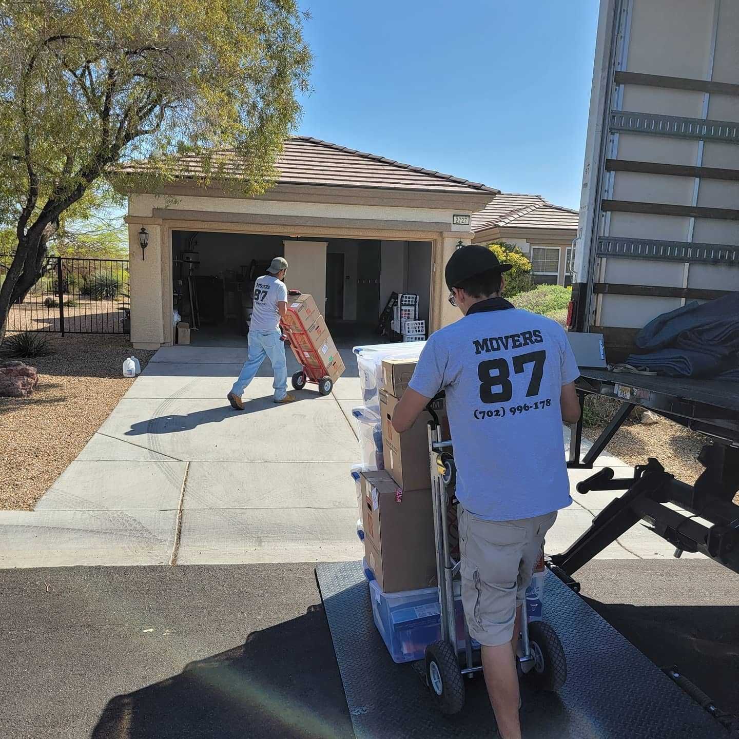 Movers unloading boxes from a home into a truck on a sunny day.