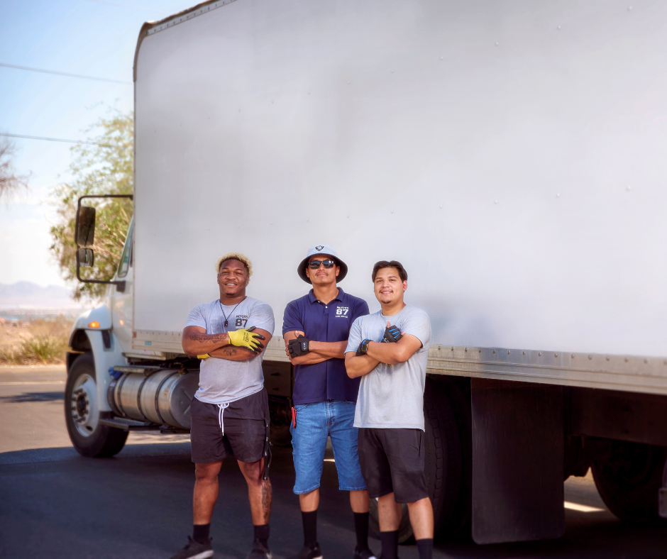 Three movers stand in front of a white moving truck. They have arms crossed, smiling in a sunny outdoor setting.