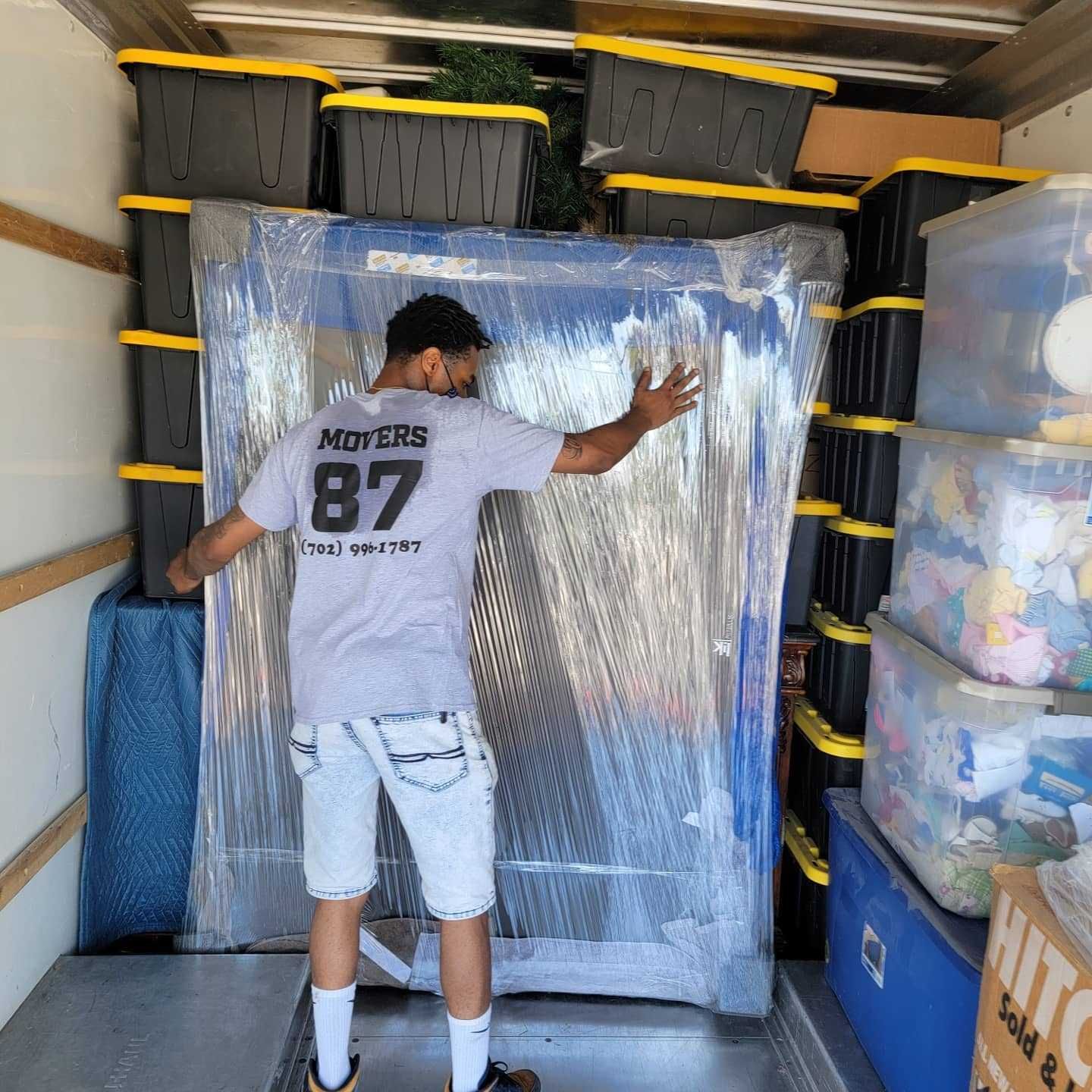 A person inside a moving truck, holding a wrapped object. Boxes fill the truck.