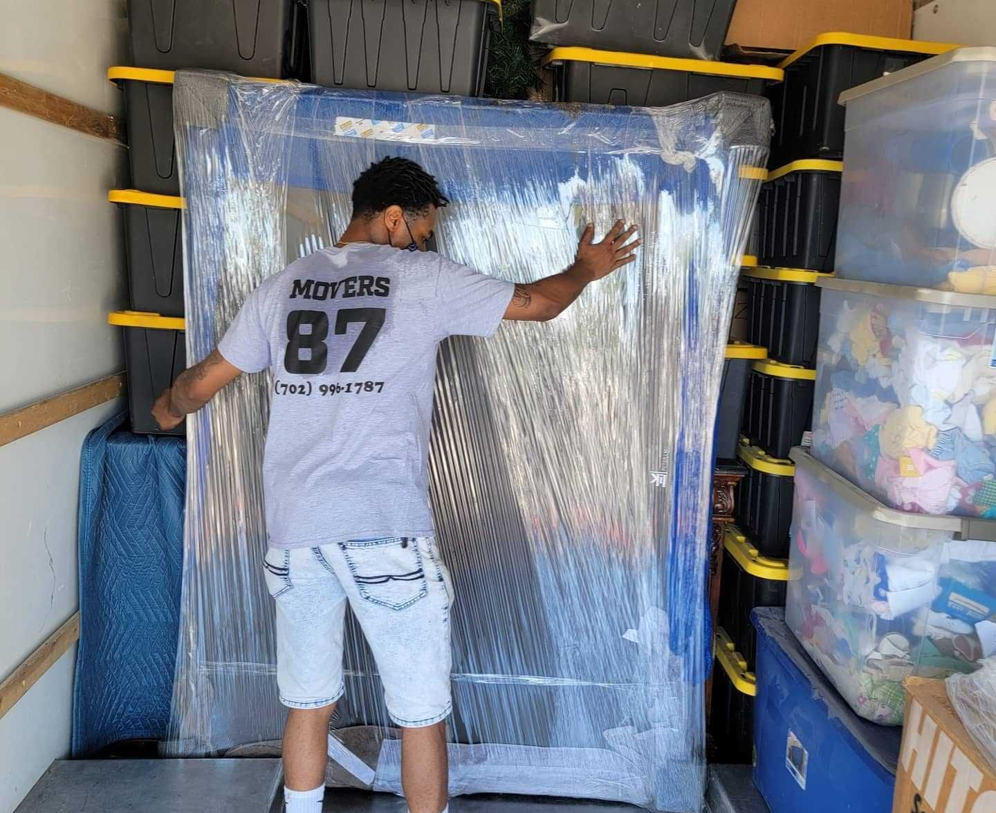 Man in a moving truck with boxes and wrapped item. He is touching the item.