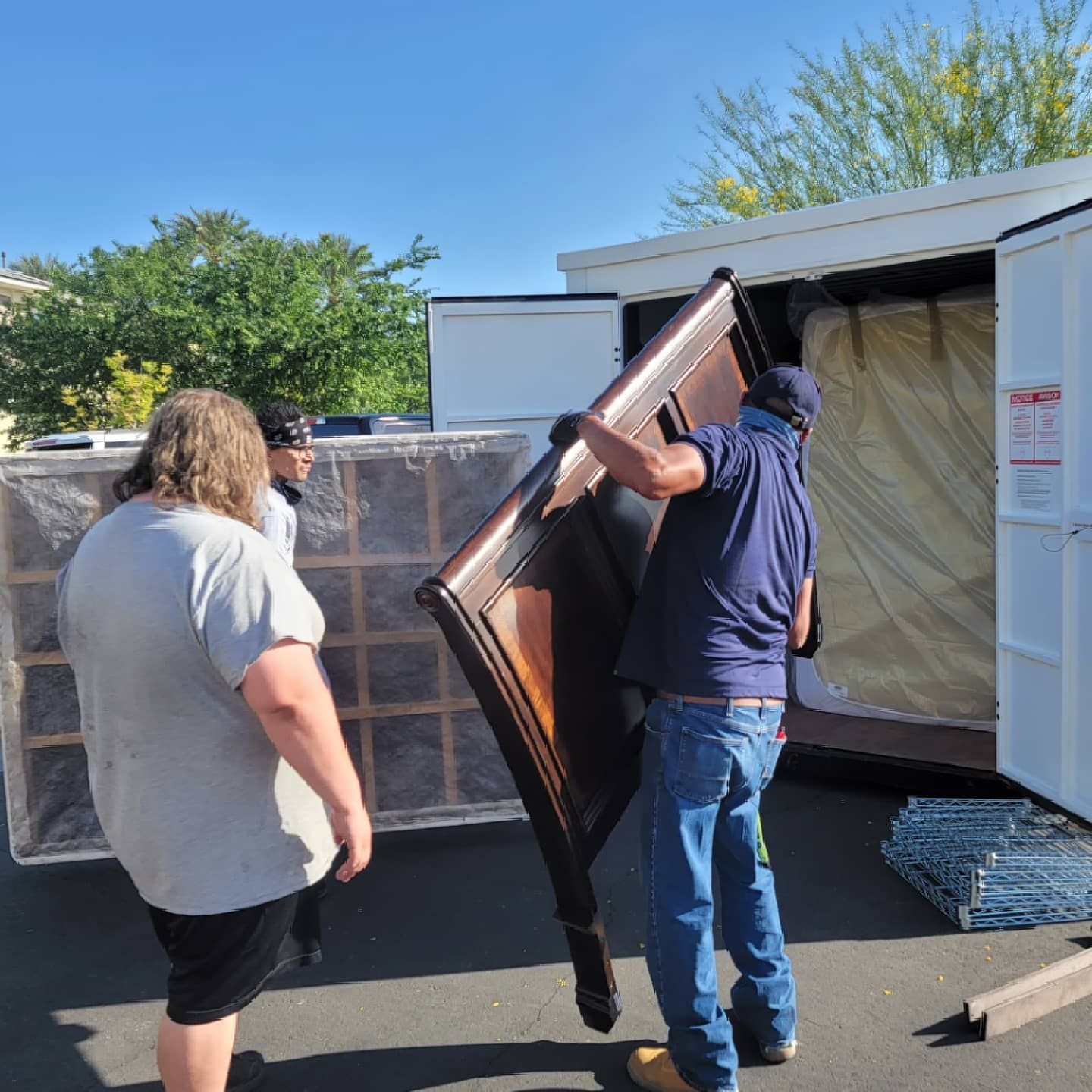People loading furniture into a white storage unit on a sunny day.