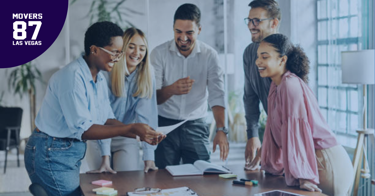Group of people looking at papers, laughing, and brainstorming around a table in an office.
