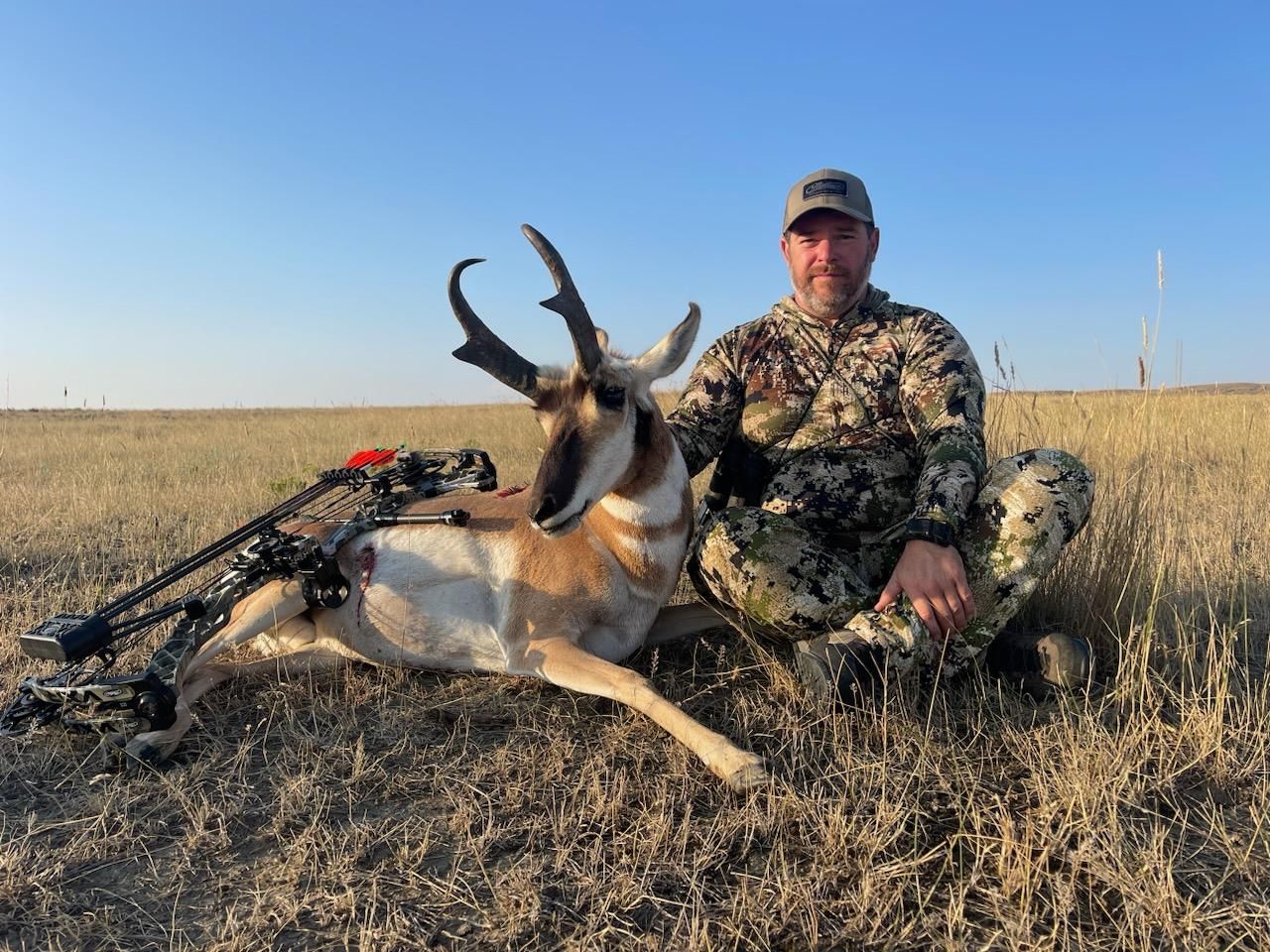 A man is kneeling next to an antelope in a field.