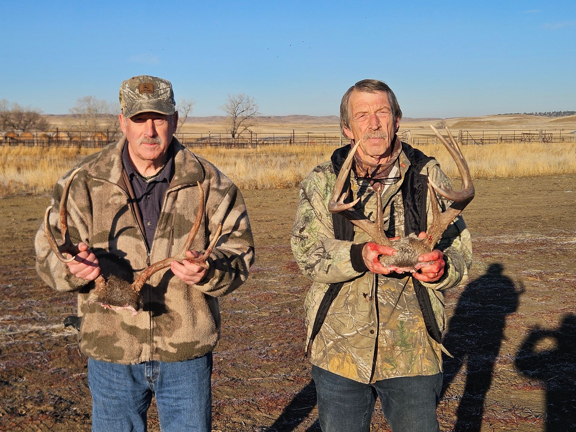 Two men are standing in a field holding deer antlers.
