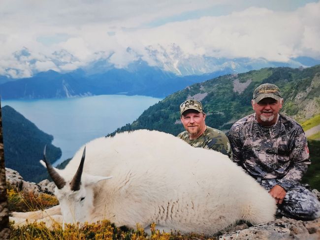 Two men posing with a dead mountain goat on top of a mountain