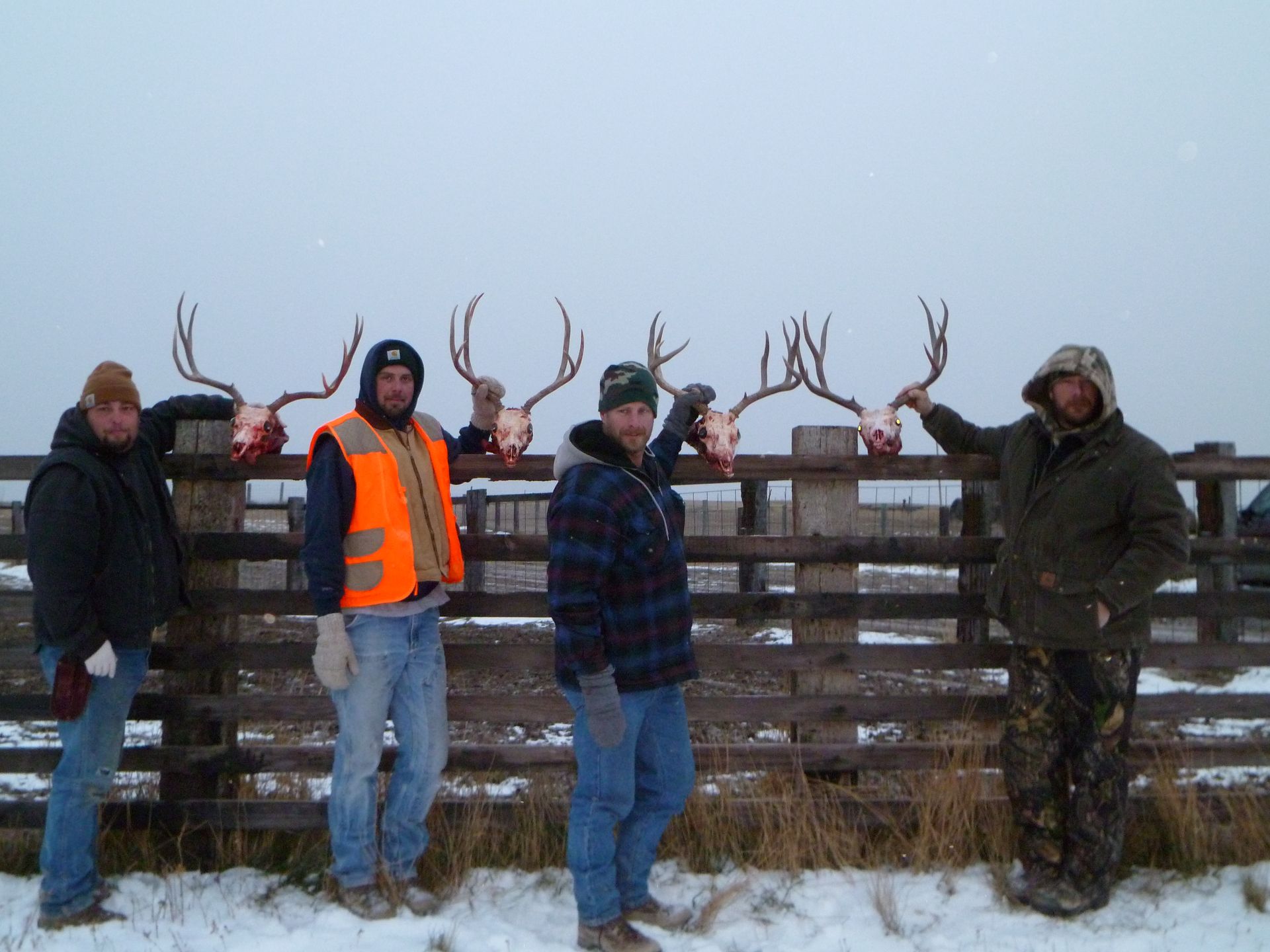 A group of men are standing in front of a wooden fence holding deer antlers