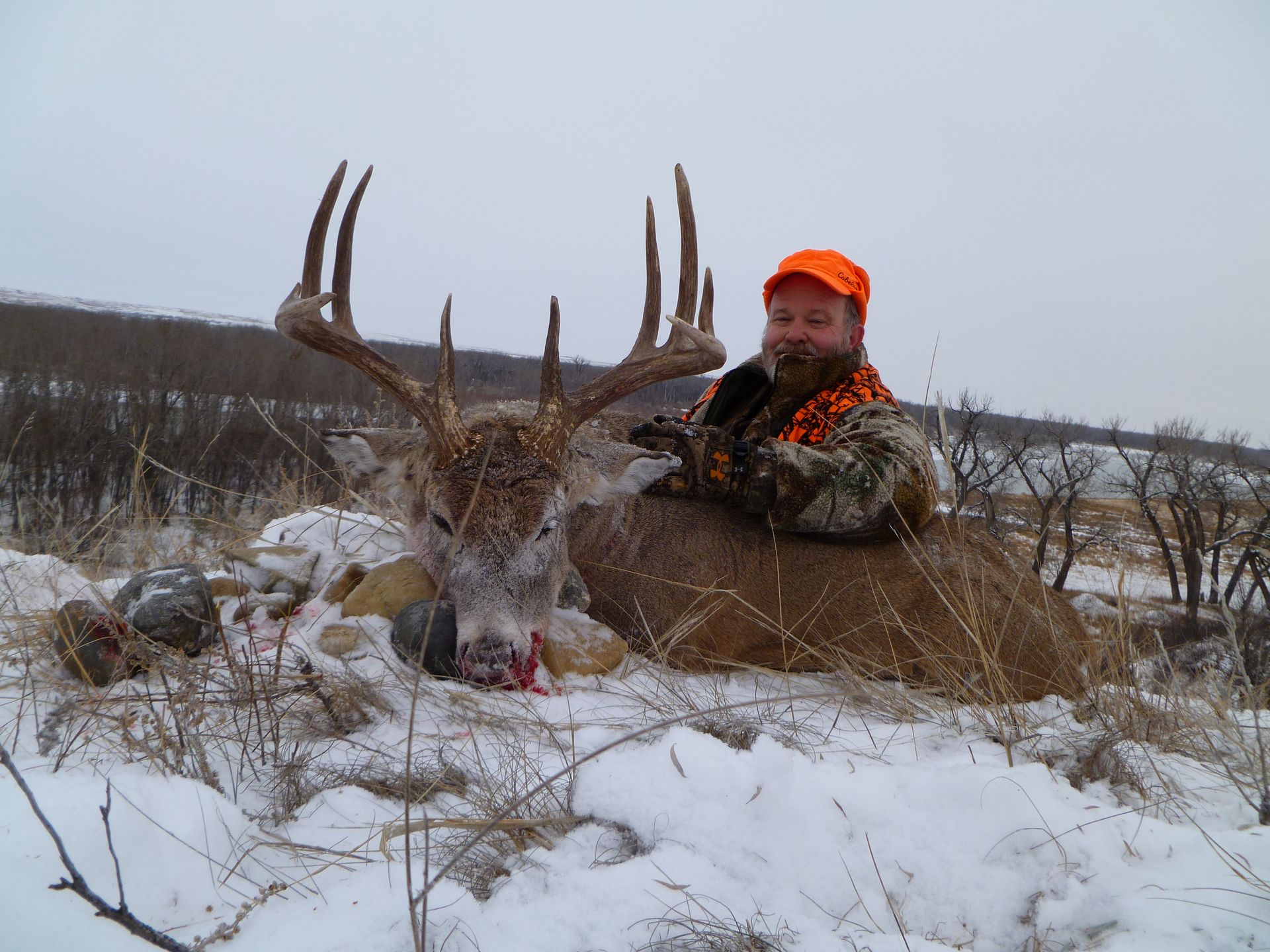 A man knelt down next to a dead deer in a snowy field