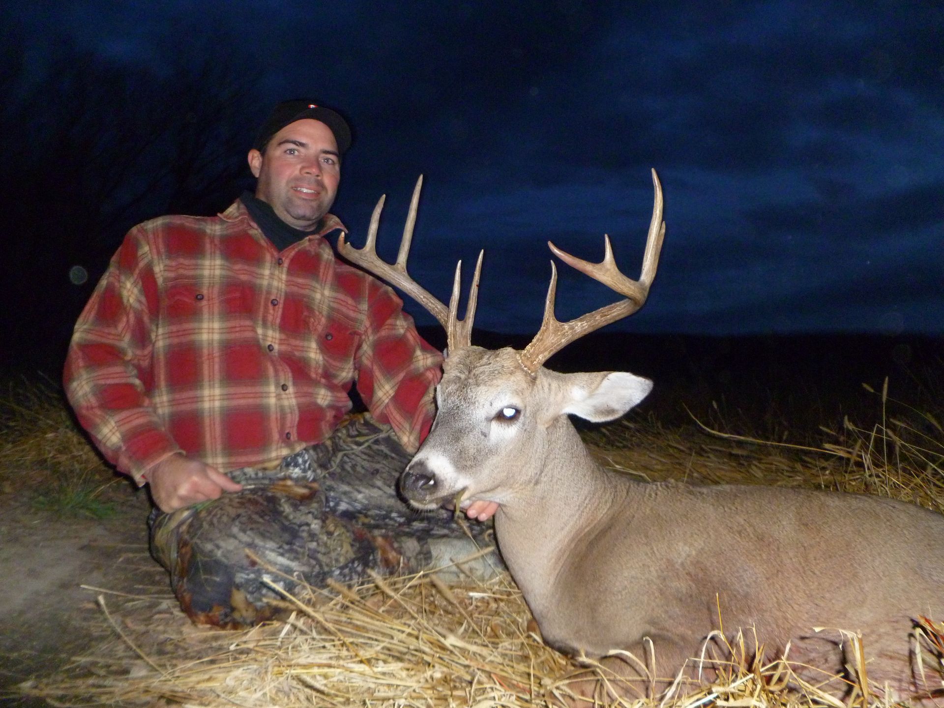A man in a plaid shirt is kneeling next to a deer