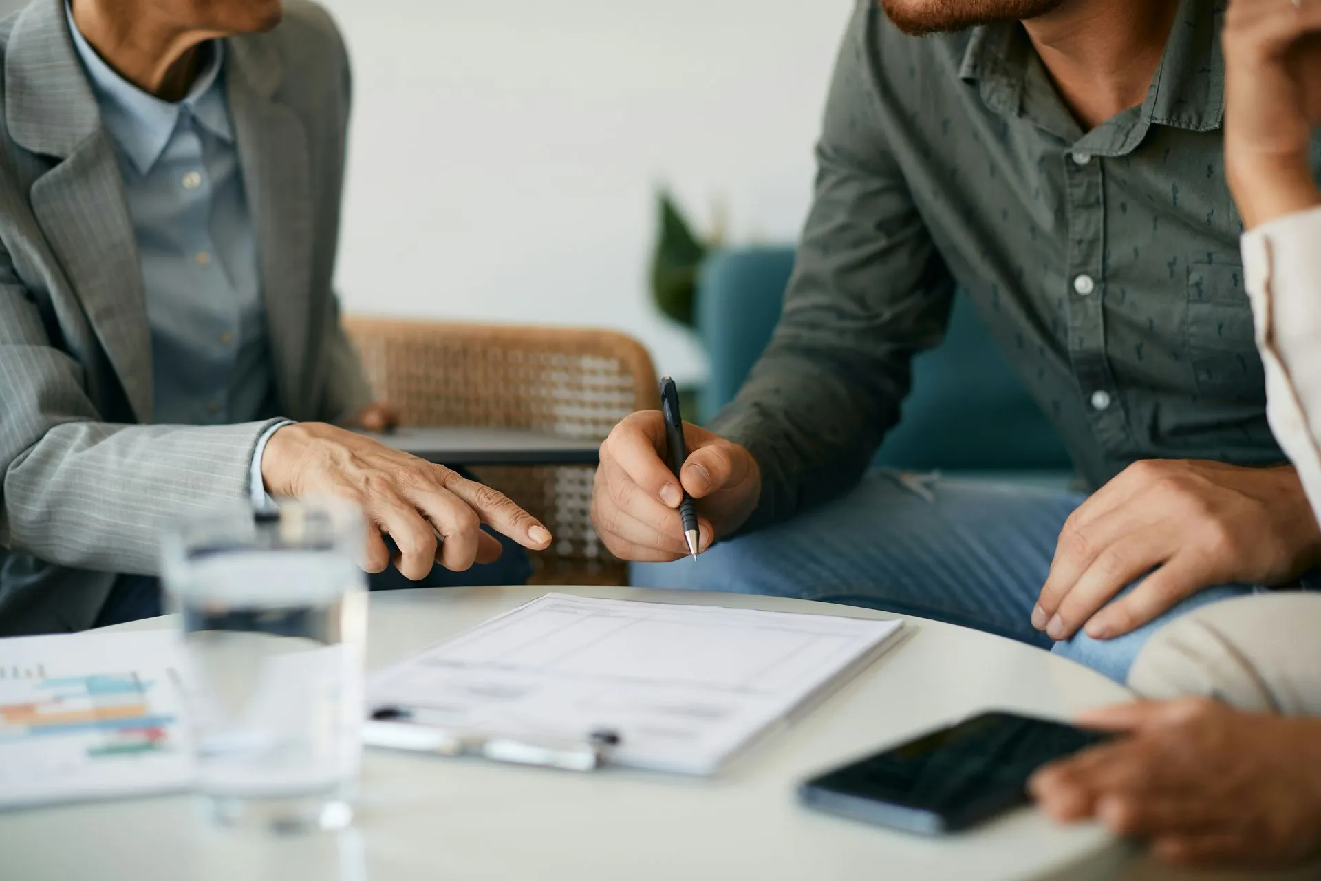 Man signing document on table, with woman pointing and another person present.