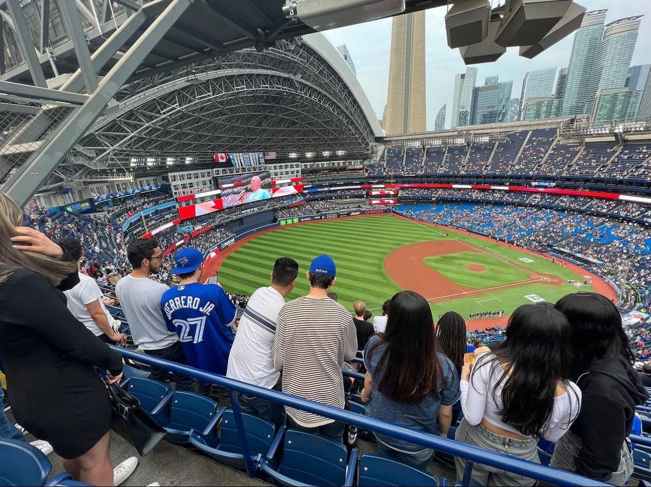 Baseball stadium filled with people watching a game. Blue seats and field, domed roof.
