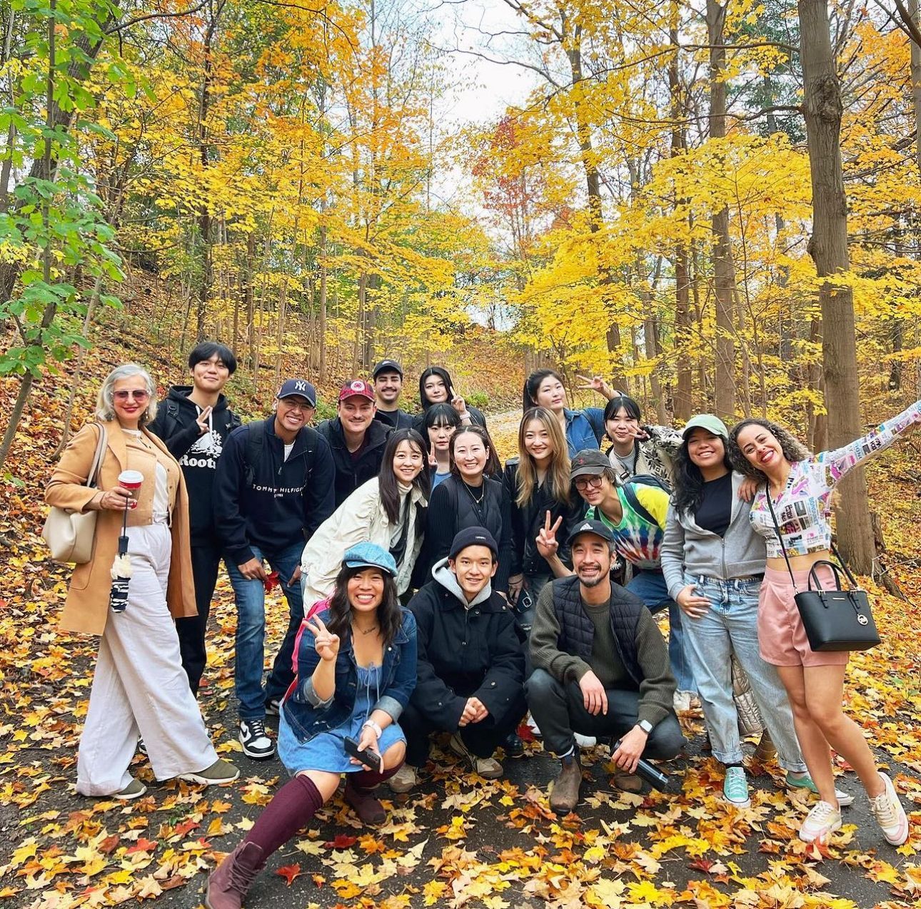 Group of people posing outdoors in fall foliage. Leaves are yellow and orange.